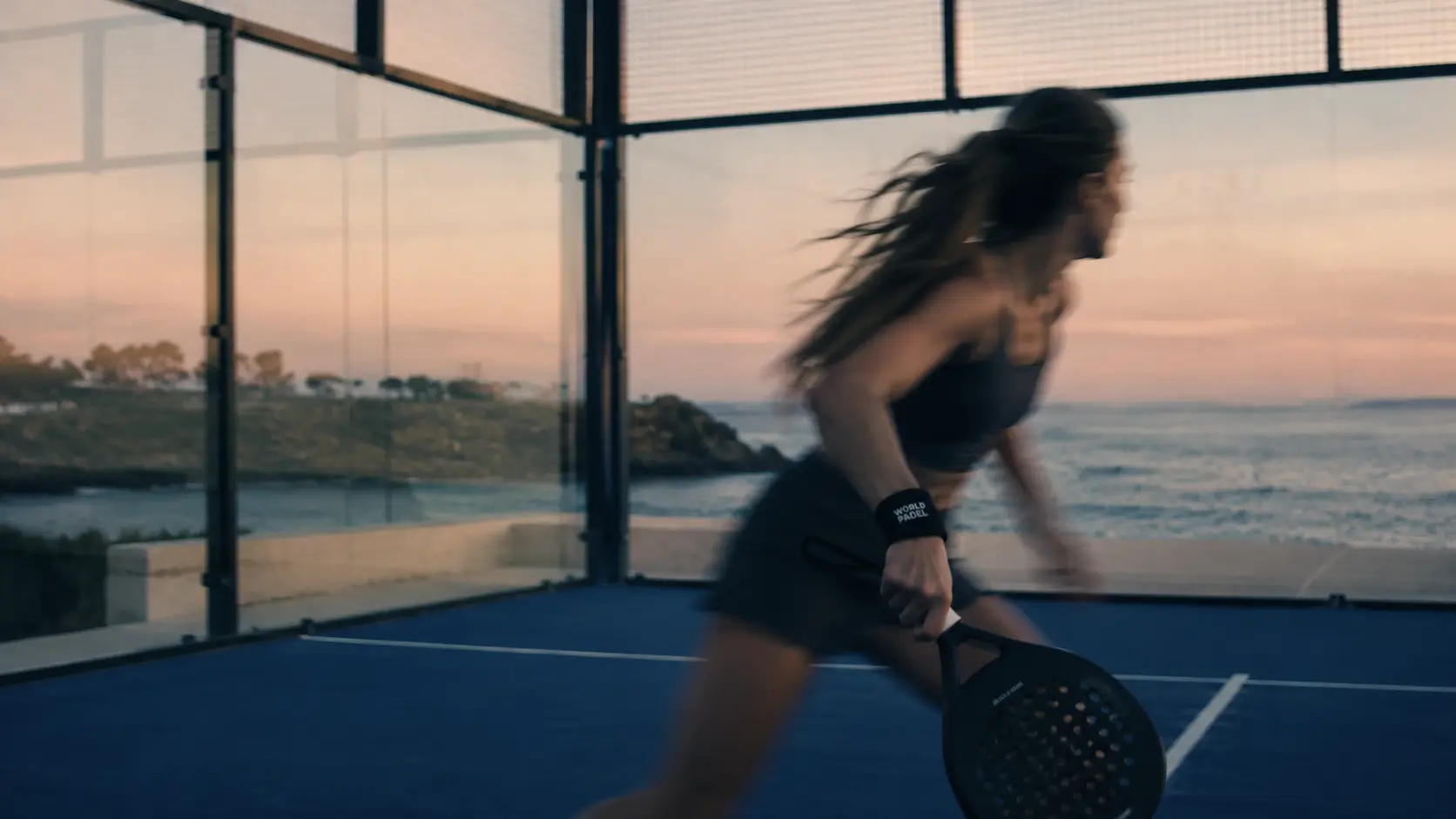 A player moving through the last of the light on Court No. 01, the sea flat behind the glass
